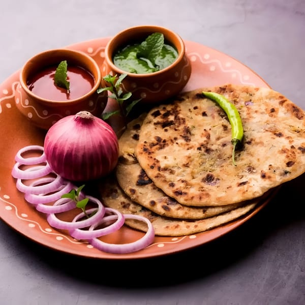 Aachi Biryani's Indian parathas with red onion, green chili, and two dipping sauces on a terracotta plate.