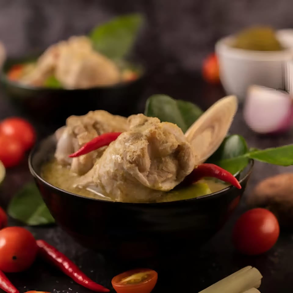 Two bowls of Aachi Biryani's chicken curry with red chilies, tomatoes, and herbs.